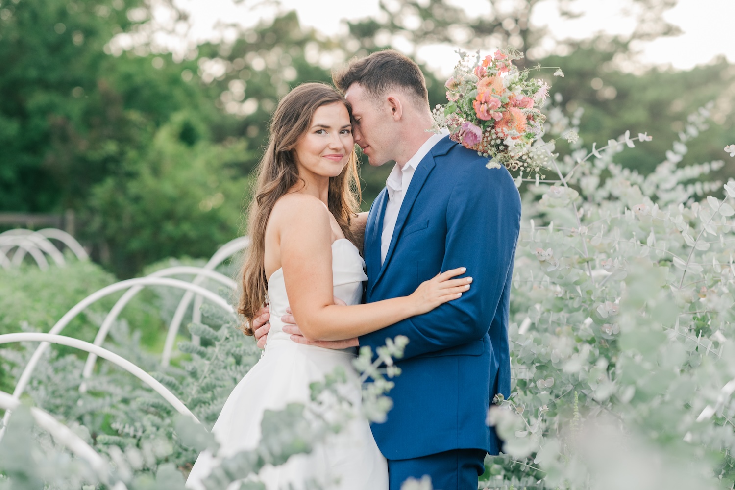 Captured by an 85mm lens a bride and groom stand in the nuzzle pose in eucalyptus farm during sunset portraits.