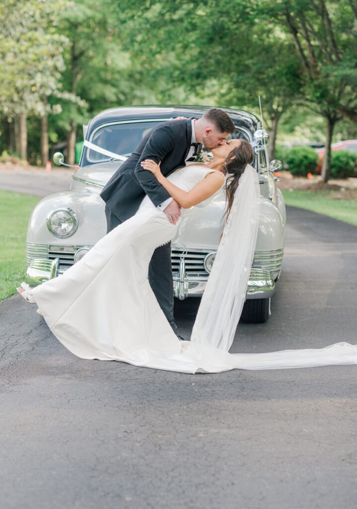 bride and groom kissing in front of their getaway car on their wedding day
