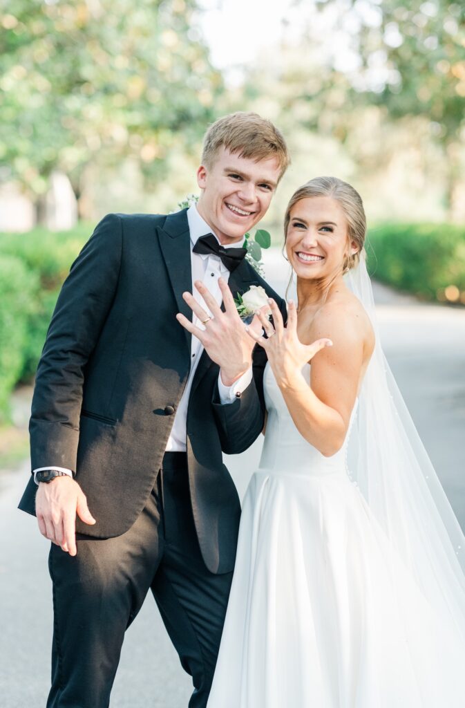 bride and groom smiling at the camera holding up their hands showing off their rings