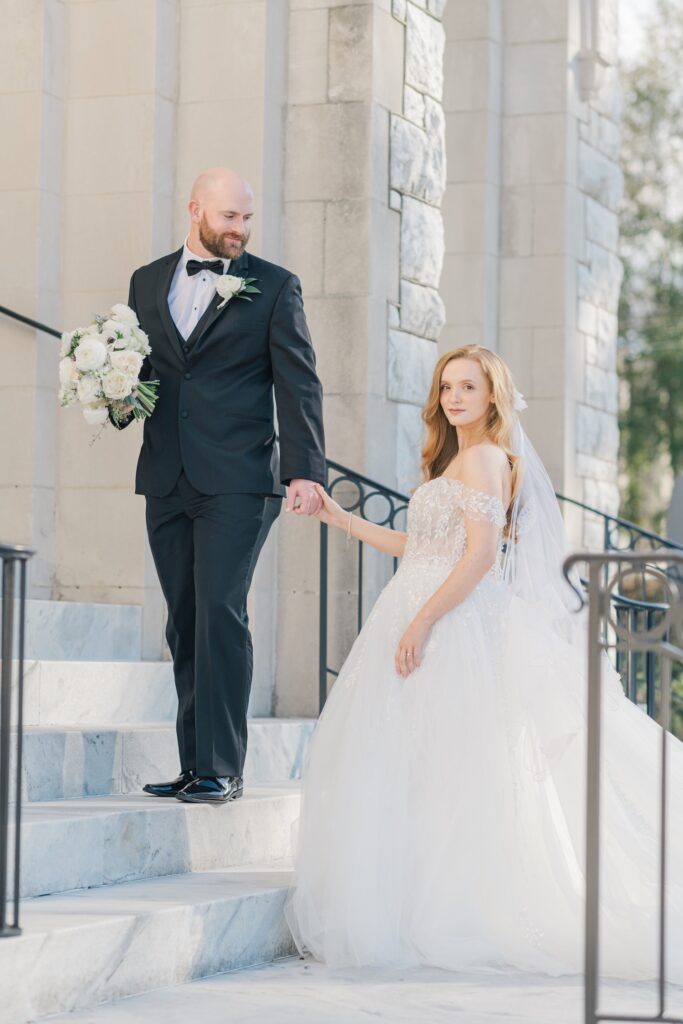 bride and groom portrait walking up the steps to the church bride is looking at the camera and groom is looking down at the bride