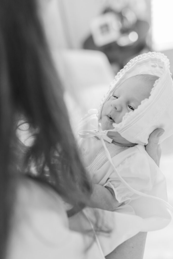 black and white photo of newborn looking up at mom wearing timeless bonnet and heirloom gown