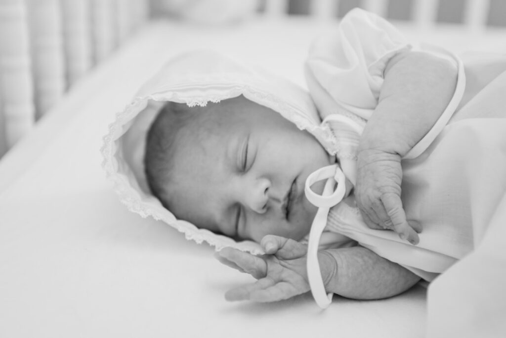 black and white photo of newborn baby girl laying in crib asleep